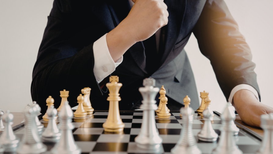 Un homme d'affaires en costume réfléchit devant un échiquier, concentré sur les pièces d'échecs dorées et argentées.