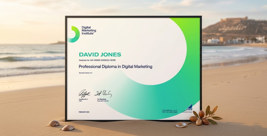 A framed Professional Diploma in Digital Marketing certificate for David Jones resting on the smooth sand of Agadir beach. In the background, there is the ocean at sunset and a distant hill. In the foreground, a few seashells and a small branch of argan nuts lay next to the certificate.