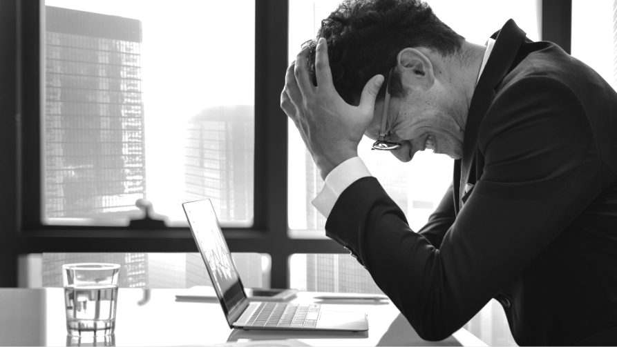 Homme d'affaires stressé et frustré se tenant la tête devant son ordinateur portable, illustrant les difficultés et l'échec d'une entreprise en marketing digital.