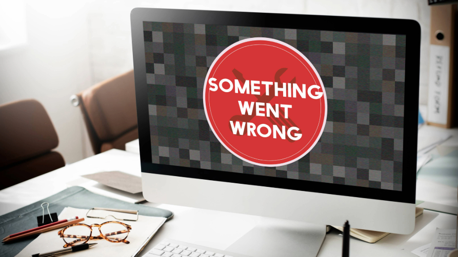 Une photo d'un bureau de travail équipé d'un iMac dont l'écran affiche un grand cercle rouge et le texte anglais verbatim "SOMETHING WENT WRONG"
